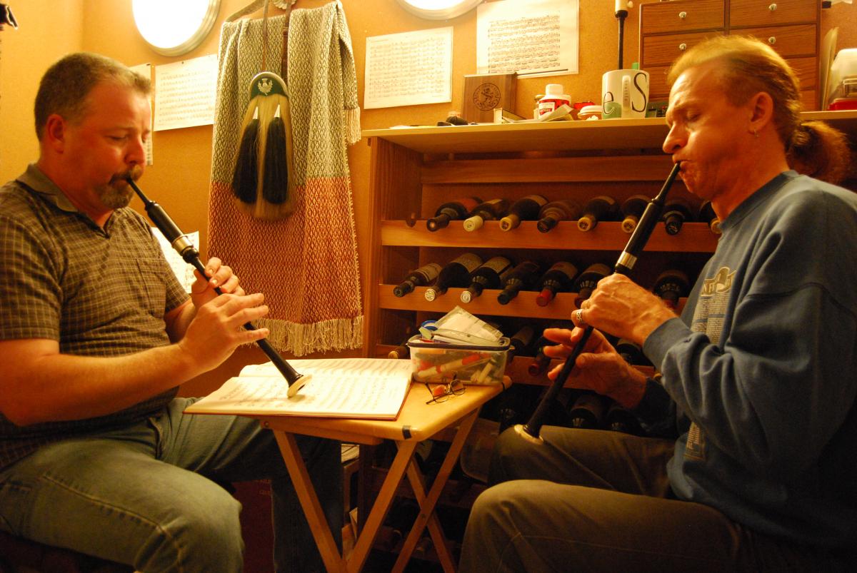 Master artist Ian Whitelaw (right) and apprentice Earl Braten.  The pipers are playing practice chanters, used to practice new tunes and complex fingering before playing them on the full bagpipe.