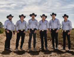 grupo Arpex standing in front of a field with blue cloudy sky above them. There are six members standing and smiling at the camera.