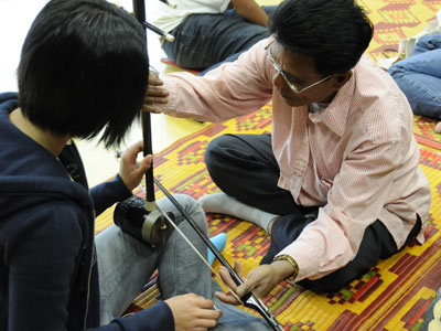 Photo of master musician Chamroeun Ploy Ngam demonstrating to students in Oakland how to play the "tro" 