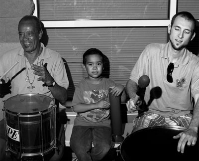 Photo of master pandeiro drummer Carlos de Oliveira, aka Carlinhos Pandeiro de Ouro playing with his 2010 apprentice Simon Carroll, with Robert, age 8, a Summer Nights Samba student.