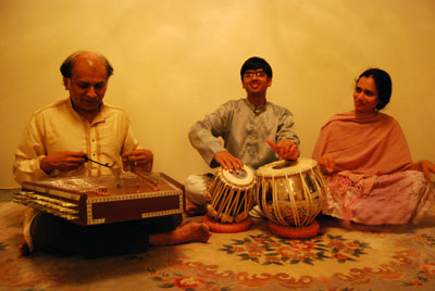 Master musician Arshad Syed (left) plays santoor to train apprentice Vikas Yendluri (center) to accompany him on tabla while Yendluri’s mother Laxmi Yendluri enjoys the extemporaneous performance in Syed’s home studio in Fremont.  In the course of the tabla apprenticeship, Syed would regularly play an unspecified raag on the santoor for Yendluri to accompany in order to mimic real life music accompaniment situations.  As Syed improvises on the raag, Yendluri must find proper times to enter in order to match his guru, and to develop appropriate improvised tabla solos.